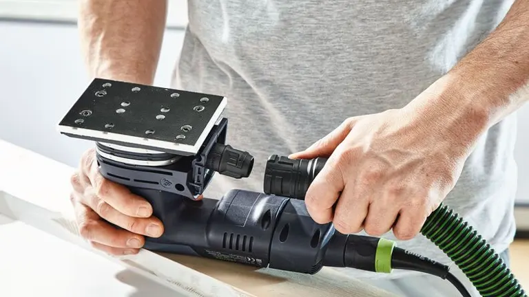 Person holding the Festool RTSC 400 Orbital Sander and ready to put the hose 