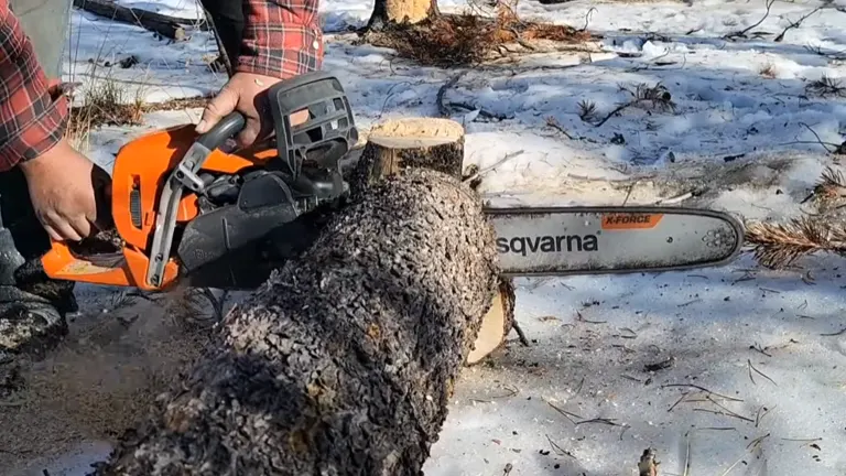 Person cutting log using Husqvarna 545 Mark II Chainsaw in a snow area