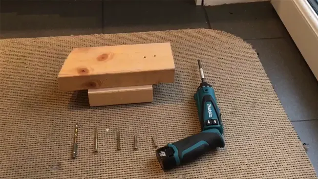 Makita cordless driver-drill with screws and wood on a textured mat.
