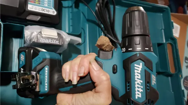 Hand gripping a Makita FD07R1 cordless drill in its case with battery and charger.