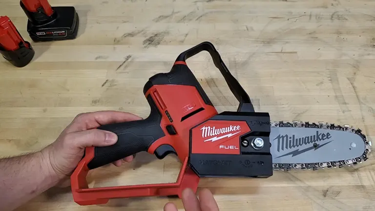 Person touching Milwaukee M12 FUEL Pruning Saw in the table with 2 battery beside of it 