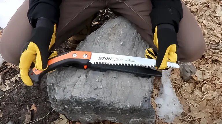 Person wearing yellow gloves demonstrating the Stihl PS 60 pruning saw on a rock outdoors