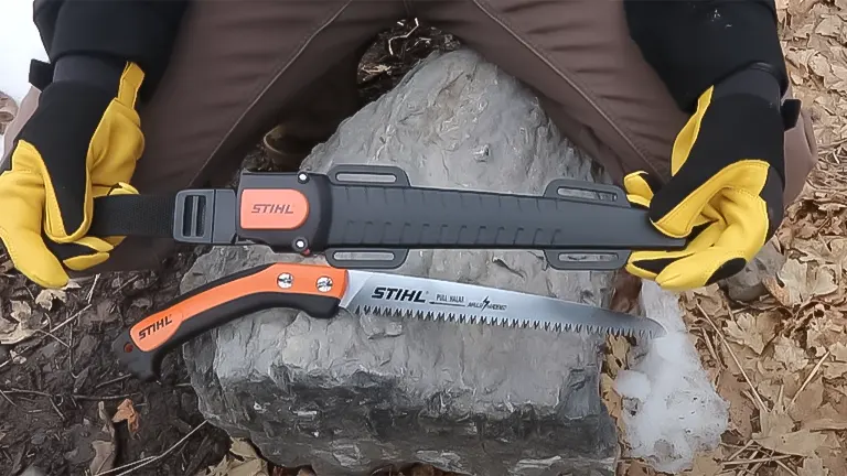 Person wearing gloves holding a Stihl PS 60 pruning saw with its sheath on a rock, ready for a review demonstration