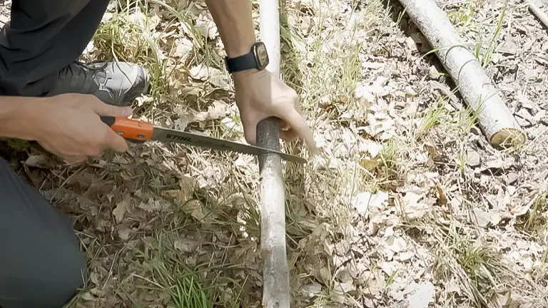 Individual using the Stihl PS 60 pruning saw to saw through a log on the forest floor, showcasing the tool in action