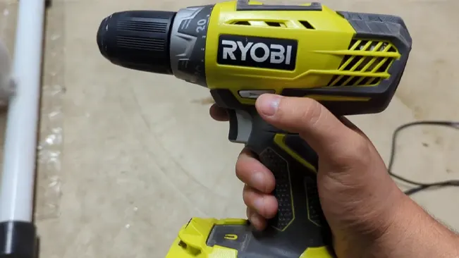 Hand holding a Ryobi P252 drill/driver in a workshop setting.