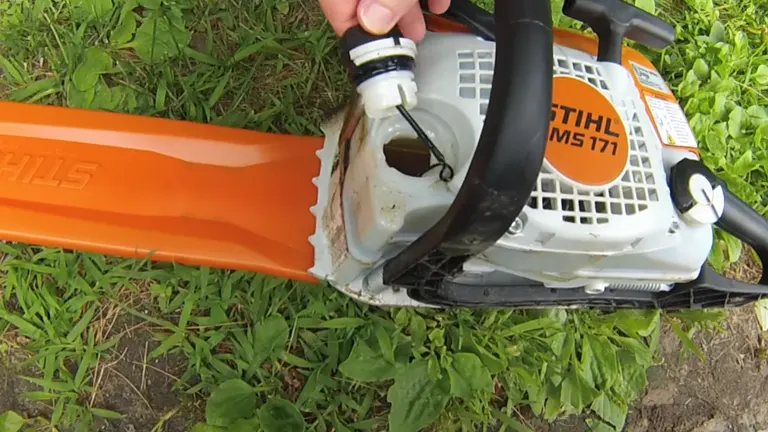 Person open the oil tank of the STIHL MS 171 Chainsaw laying in the grass