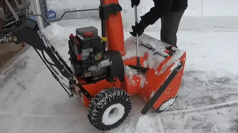 Person cleaning Snow Blower using Snow Brush