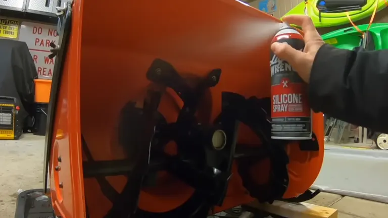 Person spraying silicone in auger housing of the snow blower