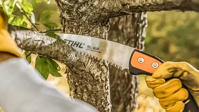 Hands in yellow gloves using a Stihl PS 90 saw on a tree branch
