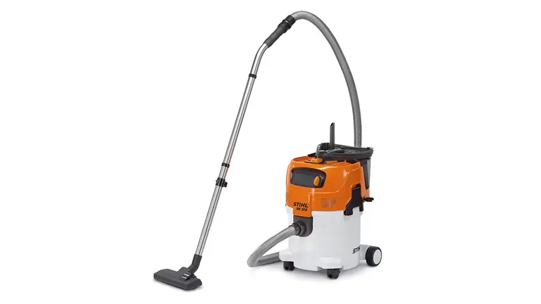 Stihl SE 122 canister vacuum cleaner with orange and white color scheme, featuring a long hose and metal wand attached to a floor nozzle