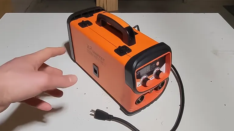 A hand pointing at an orange XR MARKET 150Amp Dual Voltage Welder Machine on a white table