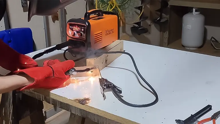 Hand in red welding glove operating the XR MARKET 150Amp Dual Voltage Welder, with visible sparks on metal