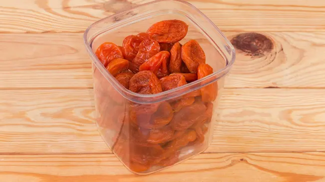 Dried smoked apricots in transparent open container on a wooden rustic table