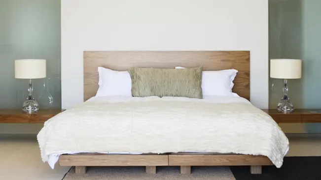 Neatly made bed with white bedding and two modern lamps on a wooden headboard