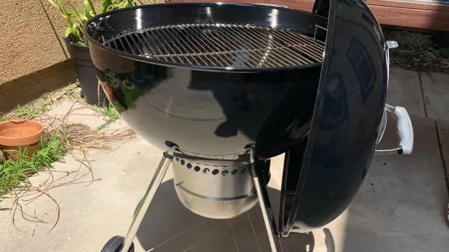 New charcoal grill in a backyard with a wooden fence and greenery in the background