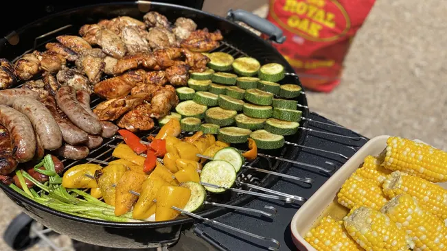 Barbecue grill filled with a variety of meats and vegetables, including sausages, chicken wings, zucchinis, and bell peppers.