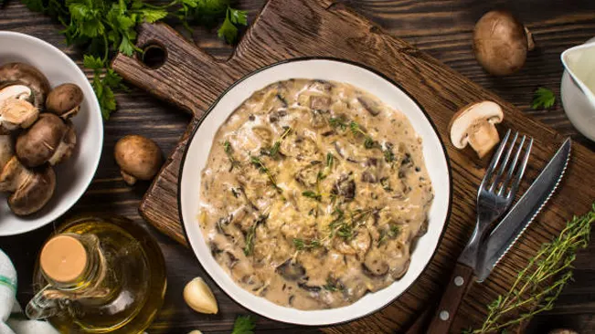A plate of creamy mushroom stroganoff garnished with herbs, surrounded by ingredients on a wooden table.