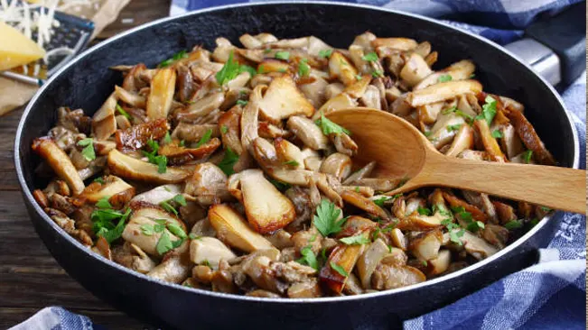 A sautéed mix of sliced mushrooms in a pan, garnished with parsley.