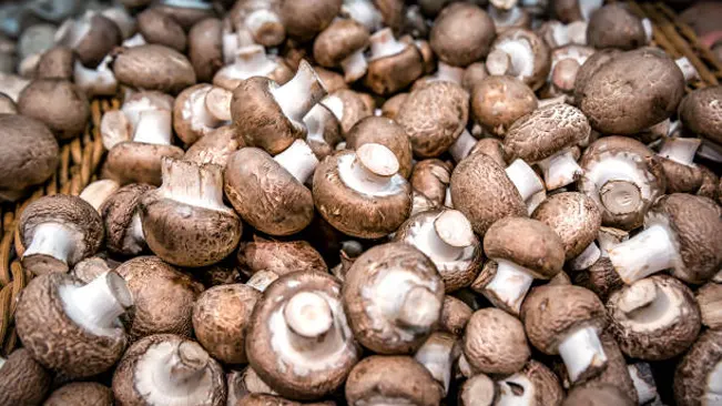 A heap of cremini mushrooms with brown caps and white stems, closely packed together.