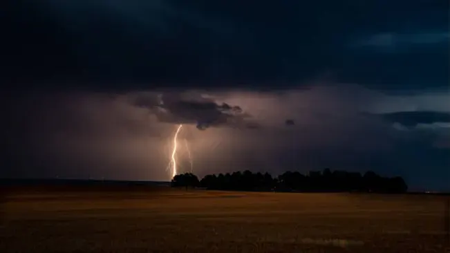 Lightning striking a field under a stormy sky, representing a natural cause of wildfires.