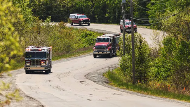 Emergency vehicles, including fire engines and support vehicles, en route on a winding road, depicting effective response tactics to a crisis situation.