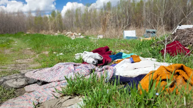 Discarded clothing and fabric lying on grass, potentially illustrating a human-made fire hazard that could lead to spontaneous combustion and wildfires.