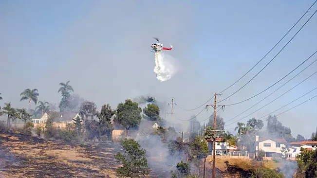 Helicopter dropping water over a wildfire near residential area.