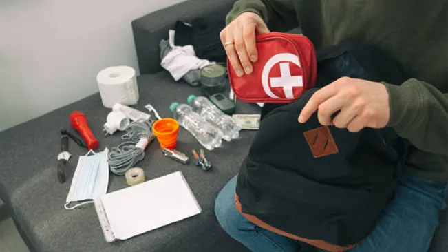 Person assembling an emergency medical kit with various supplies.