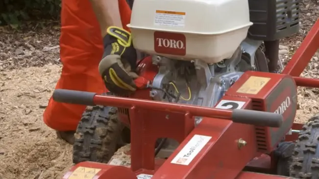 person in bright orange attire operating a red and white TORO machine on a surface covered with wood chips