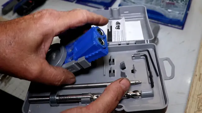 person holding a blue pocket hole jig over an open toolkit filled with various woodworking tools and accessories