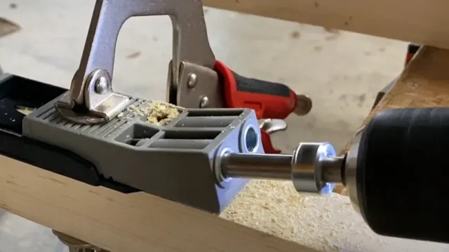 Clamp holding a piece of wood being drilled on a workbench