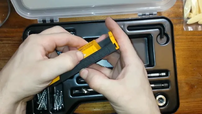 shows two hands assembling a small black and yellow tool over an open toolbox