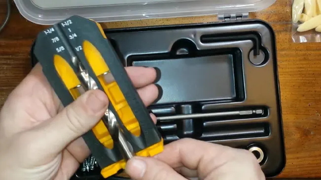shows hands holding a set of drill bits with yellow and black handles over an open black plastic case.
