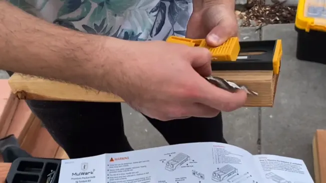 Person in floral shirt using a yellow hand tool on a wooden piece