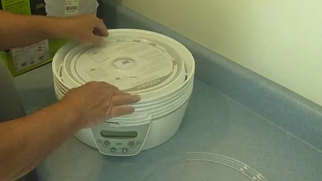 Person’s hands adjusting the lid of a white electric food dehydrator on a countertop