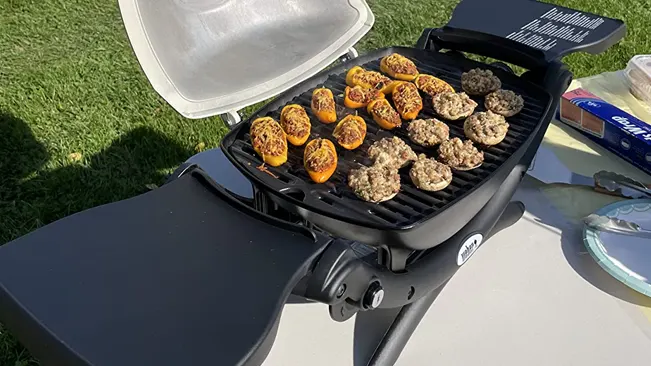 Portable barbecue grill outdoors with grilled vegetables and meat patties