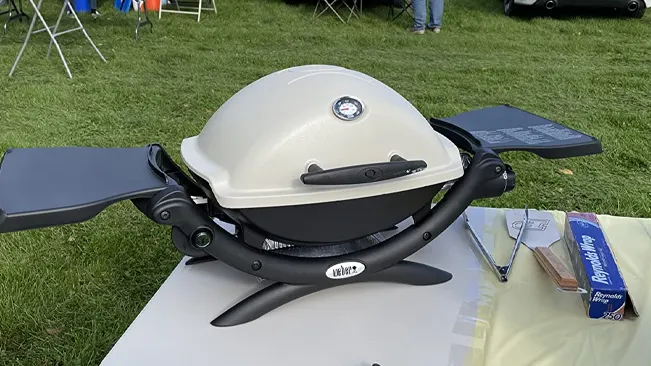 Portable Weber grill on an outdoor table with grilling accessories