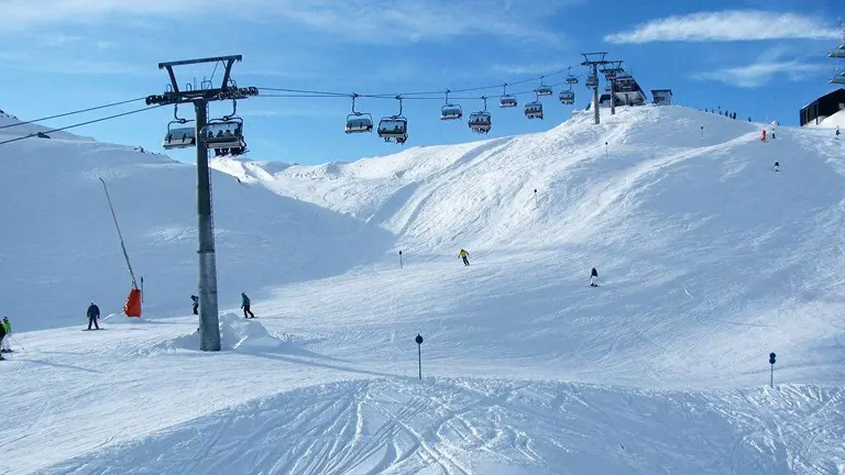 Skiers and a chairlift on a snowy mountain slope against a backdrop of clear blue skies.