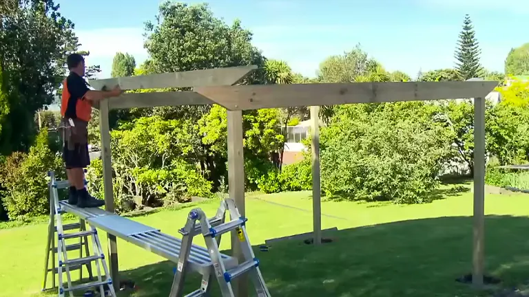 Person standing on a ladder, working on the construction of a wooden pergola in a lush garden.
