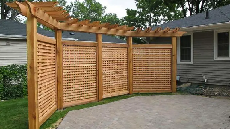Wooden pergola with lattice privacy screens attached, located on a paved patio next to a residential home.