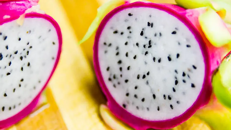 Close-up view of a sliced dragon fruit with white flesh and black seeds, showing the vibrant pink skin and a cross-section of the juicy interior.