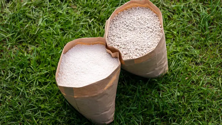 Two open paper bags on grass, filled with different types of fertilizer granules.