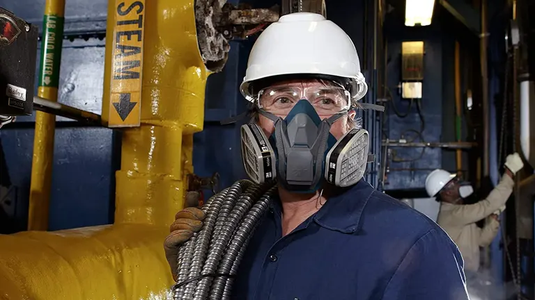 A worker wearing a full-face respirator with dual filters, working in an industrial environment, illustrating the importance of respiratory protection.
