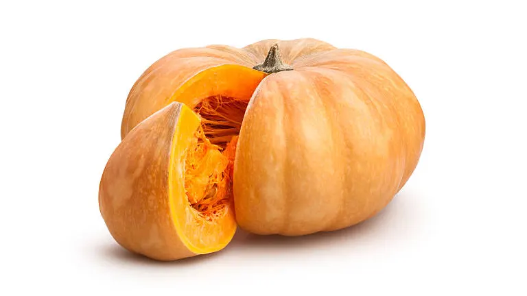 A whole tan pumpkin with a cut wedge revealing the fibrous interior and seeds, displayed on a white background.