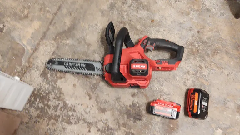 Craftsman 20V Chainsaw laying on the cement floor with 2 pieces of battery beside