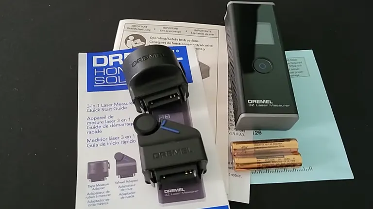 A Dremel 3-in-1 Digital Measurement Tool set up on a table with its box and included accessories such as a quick start guide, detailed manual, wheel adapter, and two AA batteries. The tool resembles a compact, modern digital device.