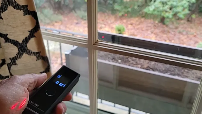 The Dremel 3-in-1 Digital Measurement Tool being used to measure the distance to a window, with the laser dot visible on the glass and the digital readout showing the measurement.