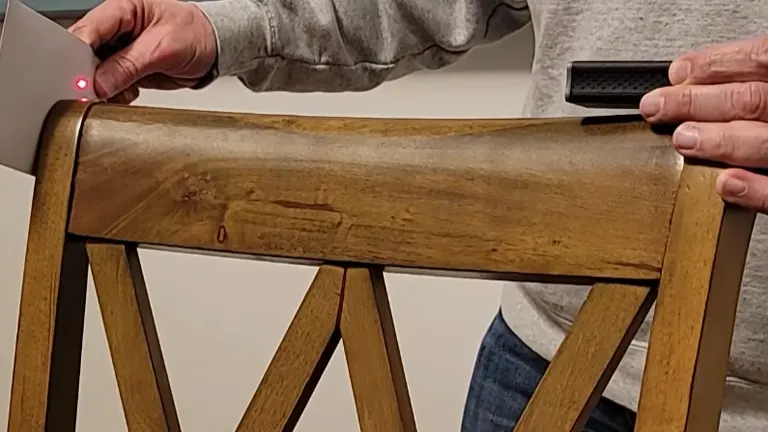 The Dremel 3-in-1 Digital Measurement Tool in use, projecting a laser onto the curved leg of a wooden chair to measure its surface.