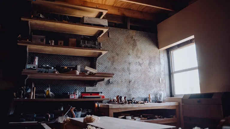 A well-organized woodworking workshop with shelves of tools and materials, a workbench with various hand tools, and natural light coming through a window.

