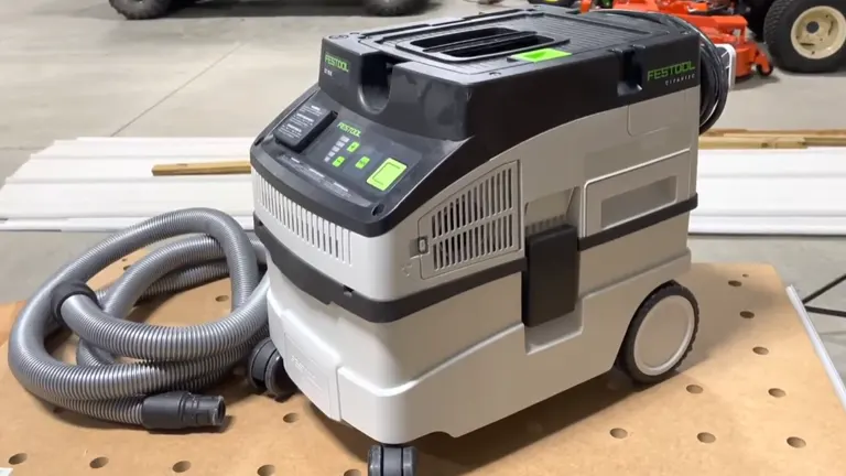 A Festool CT 15 E Dust Extractor on a wooden surface, featuring its gray and white body, green top with control panel, and connected flexible hose.